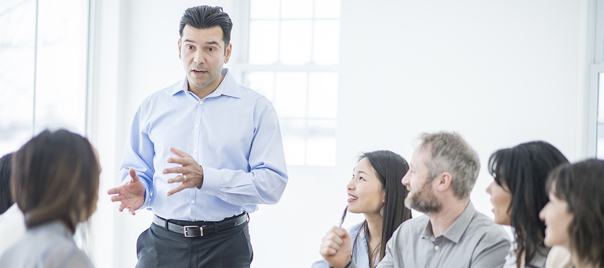 Image of a man offering a presentation to a group of people seated around a conference table