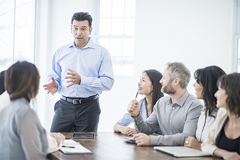 Image of a man offering a presentation to a group of people seated around a conference table